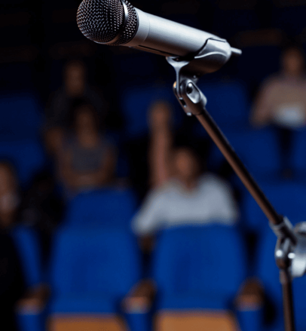 Micrófono en un escenario con audiencia visible.